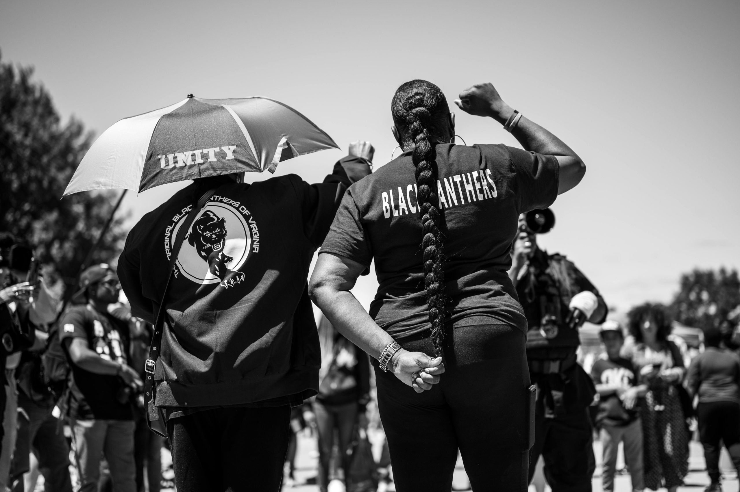 Black Panthers members raising fists in solidarity during a protest with unity umbrella.